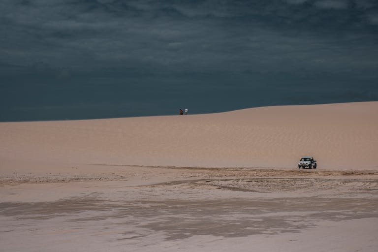 Jeep navigating the sandy dunes of Jericoacoara desert under a cloudy sky.