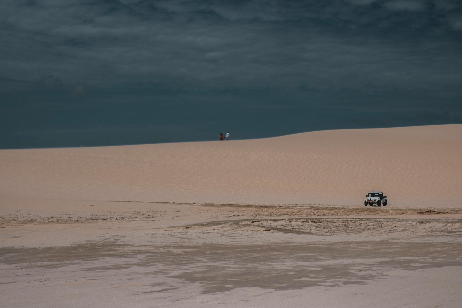 Jeep navigating the sandy dunes of Jericoacoara desert under a cloudy sky.
