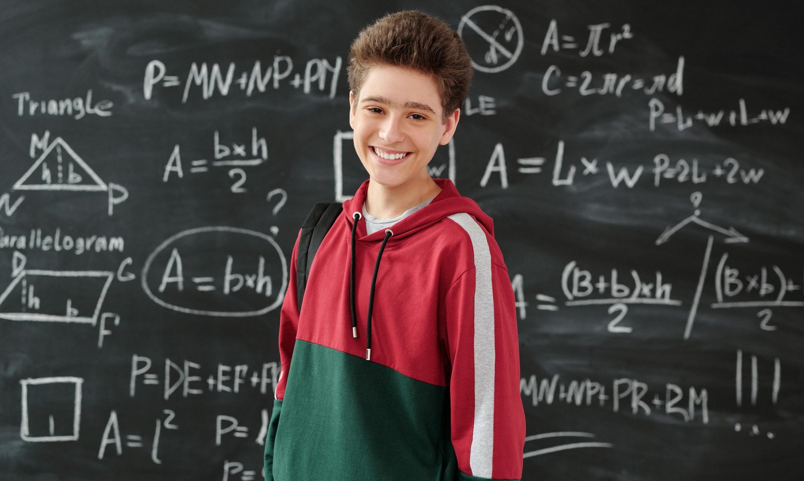 Smiling student in a classroom posing in front of a chalkboard filled with math formulas.
